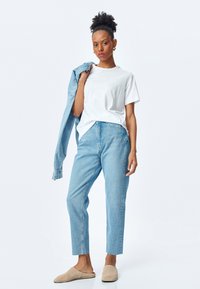 Vit bomullströja, ljusblå denimjacka, högmidjade ljusblå jeans, beige slip-on skor, mjuk textur, avslappnad passform.