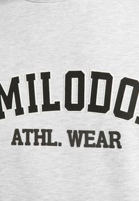 Sudadera gris con texto negro que dice "MILODOS ATHL. WEAR" en negrita. El tejido parece suave con un aspecto ligeramente texturizado.