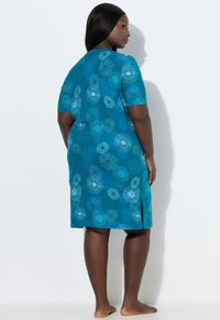 Vestido de manga corta en tela color teal con un patrón floral con detalles en azul y blanco. Incluye una abertura lateral para facilitar el movimiento.