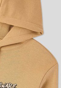 Felpa cappuccio marrone chiaro con una texture liscia, caratterizzata da un ampio cappuccio e un grafiche ricamata sul fronte. Il design è informale e accogliente.