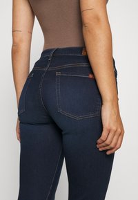 Vaqueros de mezclilla oscura con un diseño ajustado. Incluye costuras en contraste, dos bolsillos traseros y un sutil logotipo en la cinturilla.