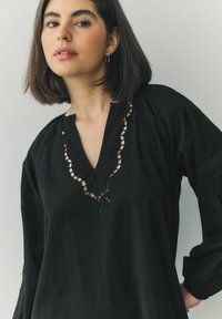 Must tuniik kergest kangast, mis on varustatud V-kaelusega ja millel on keeruline pitsdetail ning tikandid varrukatel.