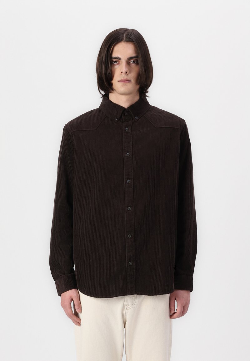 Camicia in corduroy marrone scuro con chiusura a bottoni, colletto classico e maniche lunghe. Presenta una trama a righe verticali e bottoni a contrasto.