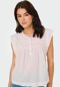 Jasnoróżowy bezrękawnik wykonany z lekkiego materiału. Posiada zapięcie na guziki, plisowane detale oraz miękką, swobodną strukturę.