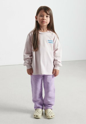 Šviesiai rožinė ilgomis rankovėmis marškinėliai su mėlynu tekstu, derinami su purpurinėmis vilnonėmis kelnėmis ir smėlinėmis klumpėmis su ventiliacijos skylutėmis. Paprastas, jaukus apranga.