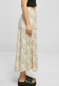 Fustă midi cu model floral în bej, cu contururi negre, talie elastică și material fluid. Asortată cu sandale negre cu platformă.