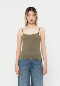 Camiseta sin mangas de color verde oliva con tirantes finos, diseño ajustado y textura suave, combinada con jeans de mezclilla azul sueltos en un ambiente informal.