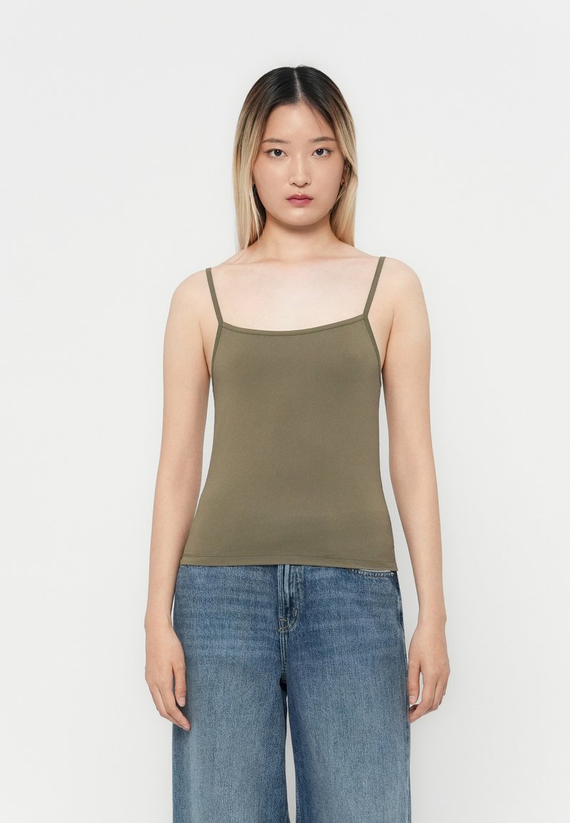 Camiseta sin mangas de color verde oliva con tirantes finos, diseño ajustado y textura suave, combinada con jeans de mezclilla azul sueltos en un ambiente informal.