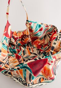Large fabric tote bag with colorful abstract leaf and geometric patterns in red, teal, orange, and black on a cream background.
