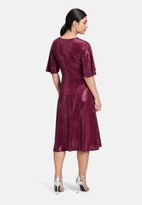 Burgundowa sukienka z krótkimi rękawami, pokryta cekinami, w kształcie rozkloszowanym, do kolan, połączona z srebrnymi sandałami na wysokim obcasie.