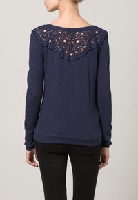 Marineblauw shirt met lange mouwen, voorzien van een kanten ontwerp aan de achterkant, een ronde halslijn en een gegolfde rand, gemaakt van zachte stof.