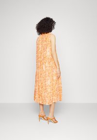 Ærmeløs orange kjole med blomsterprint og lagdelt kant, kombineret med orange hæle. Glat stof, knælængde og løs pasform.