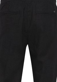 Pantalons en lin noir avec une finition texturée, dotés de deux poches arrière et d'une coupe décontractée. Couture distincte le long des poches et de la ceinture.