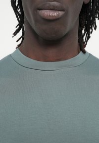 Ανοιχτό μπλε βαμβακερό μπλουζάκι με στρογγυλή λαιμόκοψη και λεία υφή. Κοντινή λήψη που δείχνει τα χείλη και την περιοχή του ώμου.