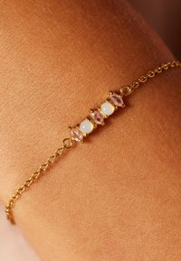 Gouden armband met drie edelstenen: twee roze marquise geslepen en één ronde opaal, met een fijne ketting en sluiting. Zachte textuur.
