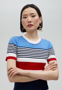 Randig stickad topp i blått, vitt, rött och marinblått med rund halsringning och korta ärmar; lager av horisontella ränder och slät textur.