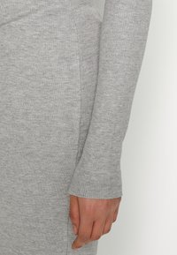 Gros plan d'une main reposant à côté d'un vêtement à manches longues côtelé gris clair en tissu tricoté doux.