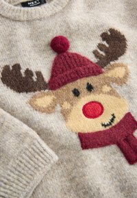 Pull beige en tricot avec un renne texturé portant un chapeau et une écharpe rouges, avec un nez rouge et des bois marron.