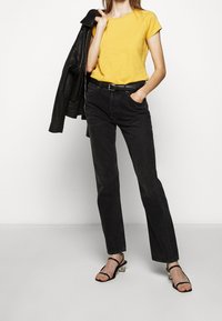 Żółta, krótka koszulka noszona z wysokimi czarnymi dżinsami. Czarna skórzana kurtka zarzucona na jedno ramię oraz czarne sandały na obcasie.