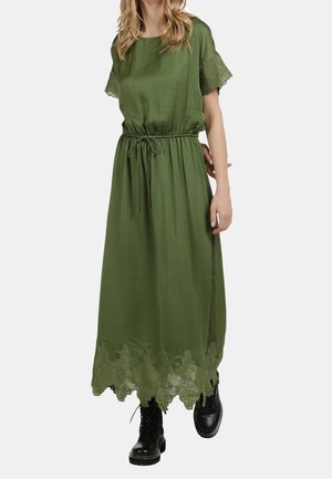 Woman wearing a midi olive green dress with lace trim sleeves and hem, cinched waist with drawstring, paired with black lace-up boots.