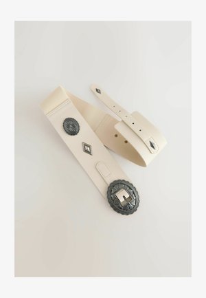 Kremast pas z teksturirano površino, ki ima veliko okrašeno kovinsko sponko in dekorativne kovinske detajle.