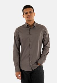Camisa de manga larga en gris oscuro, con diseño abotonado, cuello estructurado y botones a juego con un sutil detalle de logo.