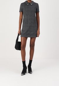 Grå rutiga minikläningen med korta ärmar och krage. Åtföljd av en svart vävd handväska och svarta klackskor med spetsig tå.