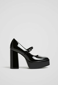 Chaussures plateforme en cuir verni noir avec une bride Mary Jane, présentant un bout rond et un talon bloc épais. Fini lisse et brillant.