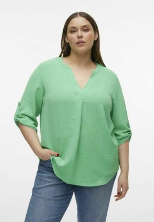 Mintgroene blouse met een V-hals en driekwartmouwen, voorzien van een gestructureerde stof en een losse pasvorm, gecombineerd met blauwe jeans.