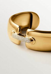 Brazalete de puño de oro con un acabado pulido y suave, que presenta un cierre decorado con pequeñas piedras preciosas blancas brillantes.