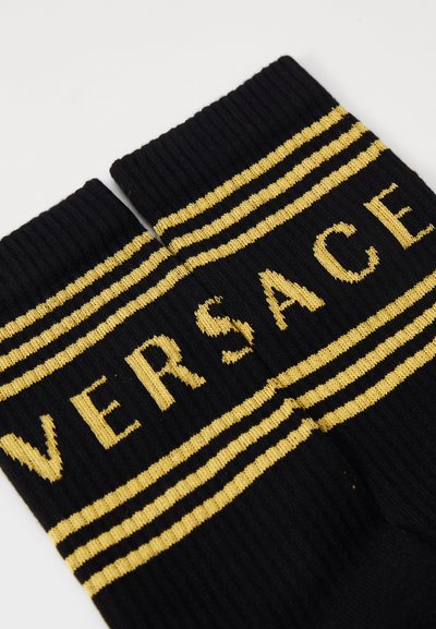 Sosete negre cu rigle, având inscriptionat cu litere aurii "VERSACE" și două dungi aurii orizontale în partea de sus. Textură moale și formă ergonomică.