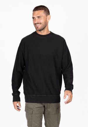Sudadera negra con relieve, de manga larga y cuello redondo. Tejido texturizado, ajuste holgado y diseño de color sólido. Combinada con pantalones cargo.