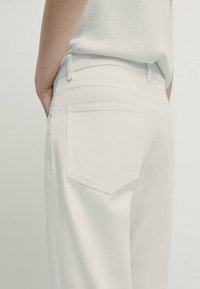 White denim pants with a high waist, straight cut, featuring back pockets and subtle stitching details. Texture appears smooth and clean.