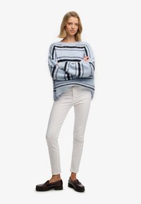Lyseblå stribet sweater med sorte og hvide accenter, kombineret med hvide slim-fit bukser og mørke loafers. Varm, strikket tekstur.