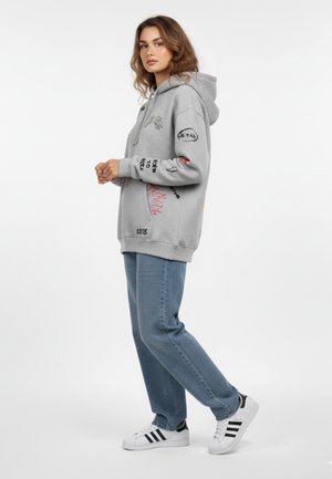 Felpa con cappuccio grigia con vari motivi ricamati colorati. Abbinata a jeans azzurri chiari e sneaker bianche con strisce nere.