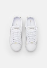 Baskets en cuir blanc avec lacets plats, accents dorés, logo sur la languette et design à rayure unique sur le côté. Texture lisse et minimaliste.