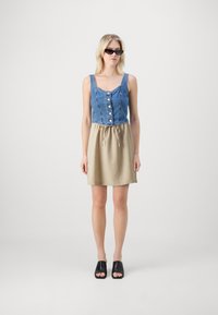 Corp haut en denim avec boutons et jupe beige à cordon. La robe présente une partie supérieure ajustée et une partie inférieure décontractée. Des mules noires complètent le look.