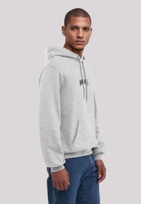Gray hoodie with drawstrings, featuring a front pocket and black text on the chest. Paired with blue denim pants. Smooth fabric texture.