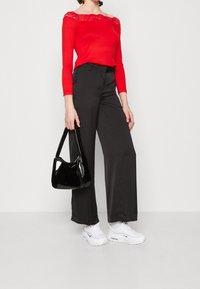 Röd långärmad topp med spetskrage, i kombination med svarta vida byxor. Accessoarer med en glänsande svart handväska och vita sneakers.