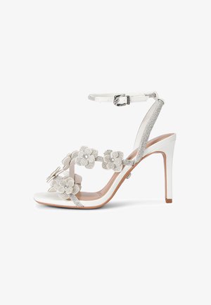 Sandale blanche à talons hauts avec bride à la cheville, décorée d'ornements floraux scintillants sur les parties des orteils et de la bride.
