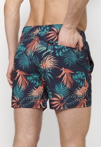 Boxeri de înot pentru bărbați din material bleumarin, cu un model vibrant de frunze tropicale în nuanțe de verde teal și corai. Talie elastică cu buzunare.