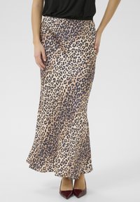 Maxi-Rock mit Leopardenmuster aus glänzendem Stoff, mit taillierter Taille und ausgestellt geschnittenem Saum. Getragen mit burgunderfarbenen High Heels.