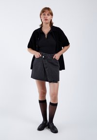 Zwarte denim rok met een wikkelontwerp, vooraan knopen en twee zakken. Gepaard met een zwarte geribde top en kniehoogte sokken.