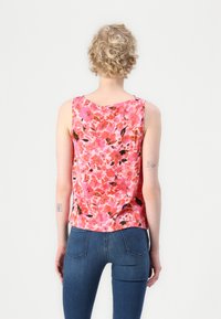 Ermeløs topp i rosa stoff med blomstermønster i nyanser av rødt, oransje og svart. Myk tekstur, buet utskjæring og avslappet passform.