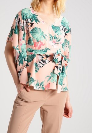 Blomstermønstret pink bluse med V-hals, korte ærmer og knyttet talje. Fremstillet i letvægtigt stof med grønne blade og blomster.