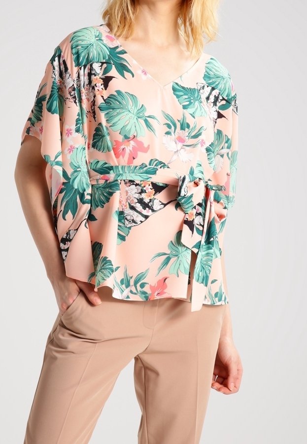 Blusa rosa a fantasia floreale con scollo a V, maniche corte e vita annodata. Realizzata in tessuto leggero con foglie e fiori verdi.
