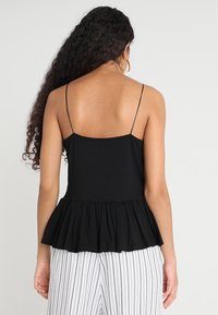 Top de camisón negro con tirantes finos y un dobladillo acampanado con volantes. La persona que lo lleva lo combina con pantalones de rayas de cintura alta.