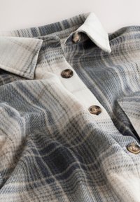 Chemise en laine à carreaux gris et beige avec grand col et quatre boutons en écaille sur la patte de devant.