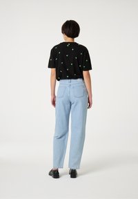 Zwarte t-shirt met kleine groene patronen, gecombineerd met lichtblauwe wijde jeans en zwarte schoenen. De outfit heeft een casual, relaxte pasvorm.