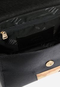 Interieur van een zwarte stoffen tas met een zakje met rits, gladde textuur, gouden ritsuiteinde, voering met bedrukt logo en een kurken accent aan de onderkant.